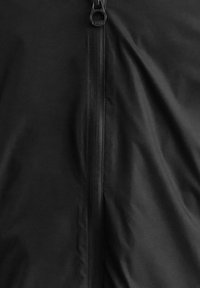 Giacca nera con cerniera caratterizzata da una texture liscia e opaca, con chiusura centrale a zip, che enfatizza un design lineare e dettagli minimi.