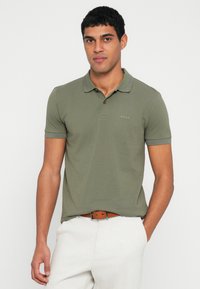 Oliwkowa koszulka polo z kołnierzykiem, krótkimi rękawami i subtelną lamówką na ramionach. Na piersi znajduje się małe logo "BOSS".