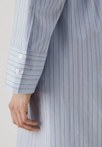 Camicia a maniche lunghe azzurra chiara con righe verticali bianche, polsini abbottonati, tessuto in cotone liscio e vestibilità sartoriale.