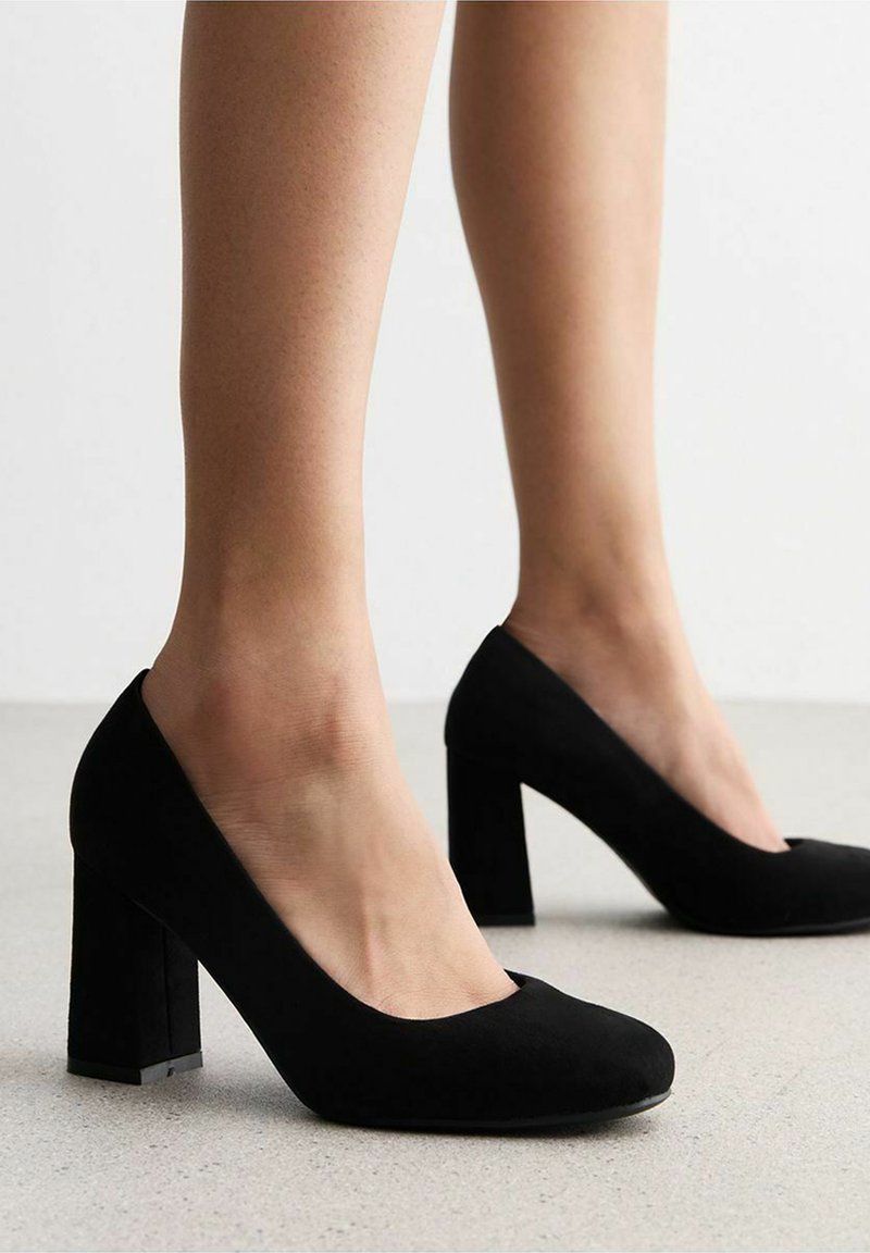 Scarpe con tacco alto in suede nero, con punta arrotondata e tacco a blocco. Le scarpe hanno una texture liscia e un design minimalista.