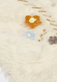 Weißer, flauschiger Stoff mit drei gestickten Blumen: orange mit gelbem Mittelpunkt, hellblau mit gelbem Mittelpunkt und grau mit rotem Mittelpunkt.
