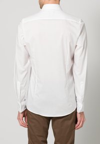 Witte lange mouw knoopsluiting shirt met een klassieke kraag, een gladde textuur en een afgeronde zoom, weergegeven vanaf de achterkant, gecombineerd met bruine broek.