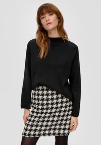 Zwarte trui met hoge hals in combinatie met een rok tot op de knie met een zwart-wit houndstoothpatroon. Getextureerde stof.