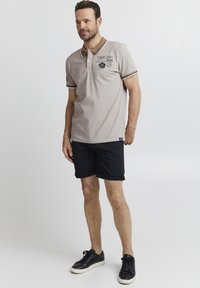 Polo gris claro con acentos negros, dos botones, logotipo bordado, combinado con pantalones cortos negros y zapatillas negras. Ropa casual para clima cálido.