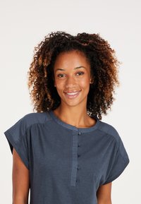 Marineblauw T-shirt met korte opgerolde mouwen, ronde halslijn en een knopenlijst met vijf knopen aan de voorkant. Zachte, lichte stof.