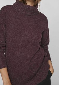 Pull à col roulé bordeaux en tissu tricoté doux et texturé, coupe décontractée et manches longues, avec un col légèrement oversize.