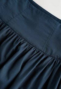 Tissu bleu marine foncé avec une texture froncée, présentant des détails soigneusement cousus le long de la ligne du buste et des plis fluides dans la partie inférieure.