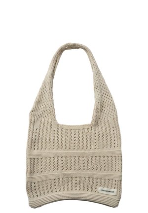 Beżowa dziergana torba typu tote z wzorem ażurowym, szerokim paskiem i małą prostokątną metką z nazwą marki w prawym dolnym rogu.