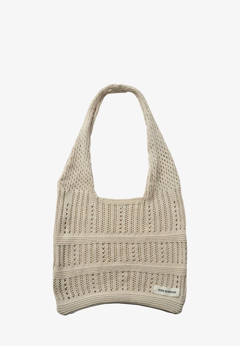 Sac fourre-tout en tricot beige avec motif à mailles ouvertes, large bandoulière, et petite étiquette rectangulaire affichant le nom de la marque en bas à droite.