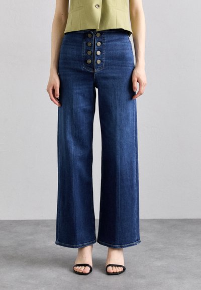 Jeans en denim taille haute, à jambes larges, dans un lavage foncé avec une braguette à boutons à l'avant comportant cinq boutons en métal. Texture lisse et finition soignée.