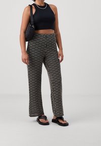 Black crop top, patterned wide-leg trousers in black and white, and black flip-flops. A quilted black crossbody bag completes the outfit.