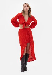 Completo rosso a due pezzi composto da un blouse cropped con le maniche voluminose e un gonnellino arricciato con una gonna alta, abbinato a stivaletti neri.