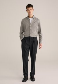 Camisa gris claro con botones y manga larga, pantalones negros con pliegues y zapatos oscuros. Incluye logo bordado en la camisa.