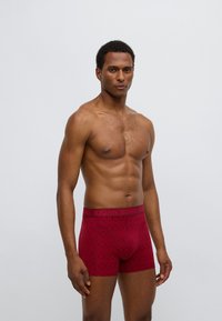 Κόκκινα μποξεράκια με σχέδιο, κατασκευασμένα από ελαστικό υλικό με ελαστική μέση διακοσμημένη με λογότυπο. Διαθέτουν γεωμετρικό σχέδιο και κοντύτερο μήκος ποδιού.