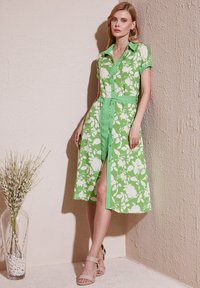 Grünes Floral-Kleid mit kurzen Ärmeln, Knopfleiste, Taillenzug und knielangem Rock. Mit einem weißen Blumenmuster und kontrastierendem Kragen.