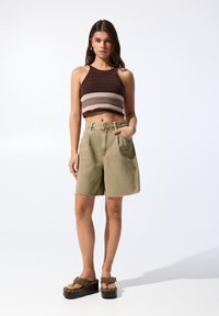 Crochet crop top dengan garis coklat dan beige, dipadupadankan dengan celana pendek denim hijau zaitun yang memiliki tepi frayed dan kantong depan. Sandal platform tebal.