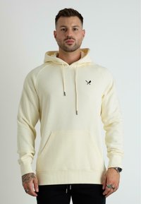 Felpa con cappuccio color crema, dotata di tasca a marsupio e un logo nero in accentuazione sul petto. Il tessuto sembra morbido con polsini a coste.