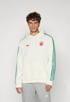 Kremowy sweatshirt z kapturem, przednią kieszenią, zielonymi paskami po bokach oraz czerwonym logo Adidas i herbem Włoch. Szare spodnie dresowe z logo na końcu nogawki.