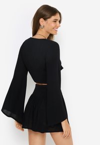 Μαύρο κοντό τοπ με μακριά μανίκια σε σχήμα καμπάνας, σετ με μαύρη φούστα με ελαστική μέση. Ελαφρύ, ρέον ύφασμα.