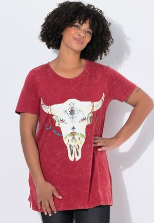 T-shirt rouge à manches courtes avec un graphique de crâne de taureau en blanc, vert et bleu. Tissu doux et texturé, ourlet incurvé, avec fentes sur les côtés.