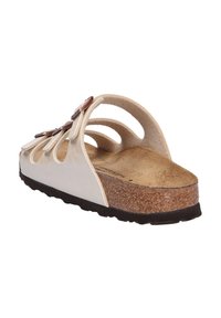 Vita lädersandal med skärdesign, texturerad korkfotbädd och svart gummisula; har en dekorativ rem med metalliska detaljer.