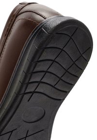 Haut de chaussure en cuir marron avec des coutures détaillées, semelle en caoutchouc noir contrastée, présentant un profil texturé pour l'adhérence et la durabilité.