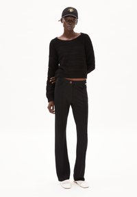 Black knitted sweater with a textured pattern, paired with black trousers featuring a button detail and pockets, finished with white shoes.