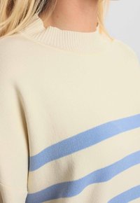 Pull crème avec des rayures horizontales bleu clair, col côtelé, texture douce et coupe décontractée. Convient pour une tenue décontractée.
