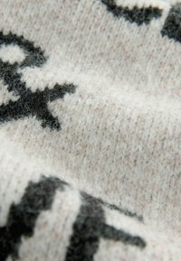 Gestrickter Wollstoff in Weiß und Hellgrau mit einem schwarzen abstrakten Muster. Weiche Textur mit sichtbaren Fasern und einem warmen Erscheinungsbild.