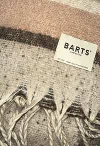 Couverture tissée en mélange de laine douce, avec des rayures beiges, roses et brunes, bordée de franges et portant une étiquette Barts.