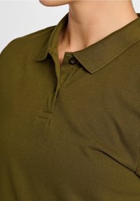 Oliven grøn polo shirt lavet af tekstureret stof, med krave, to-knaps lukning og subtile søm detaljer.