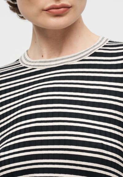 Κοντινό πλάνο ενός ατόμου που φοράει μαύρο και άσπρο ριγέ οριζόντια ριμπ πουκάμισο με στρογγυλή λαιμόκοψη.