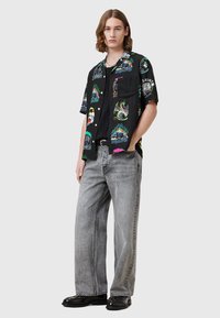 Camisa negra de manga corta con gráficos coloridos en el frente, combinada con jeans de mezclilla gris de corte holgado y zapatos negros.