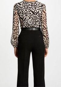 Gennemsigtig sort og creme bluse med et geometrisk mønster samt sorte højtaljede bukser med en glat tekstur og skræddersyet pasform.