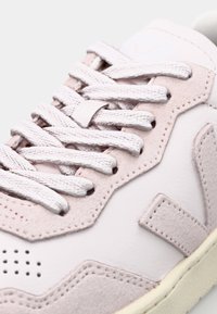 Baskets rose pâle en cuir et en daim, avec des lacets plats blancs, un bout arrondi et des perforations près du bout.