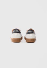 Un par de zapatillas de ante blanco de Steve Madden con suelas de goma natural vistas desde atrás sobre un fondo blanco liso.