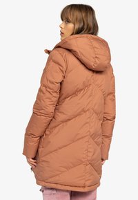 Pufferjack in roestrood, met een capuchon, diagonale stiksels en een relaxte pasvorm. Zachte textuur met ritsen aan de zijkanten.