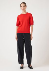 Rød strikket genser med korte ermer og rund hals, kombinert med løstsittende svarte denimjeans og svarte sko med hæl.