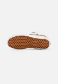 Sneaker sole in white with a textured brown rubber pattern, featuring a smooth white edge and a side panel in light tan suede.