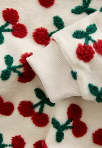 Kremna tkanina z rdečimi motivi češnjevih cvetov in zelenimi listi. Beli manšet z rebrastim vzorcem ob robu. Mehka, teksturirana snov.