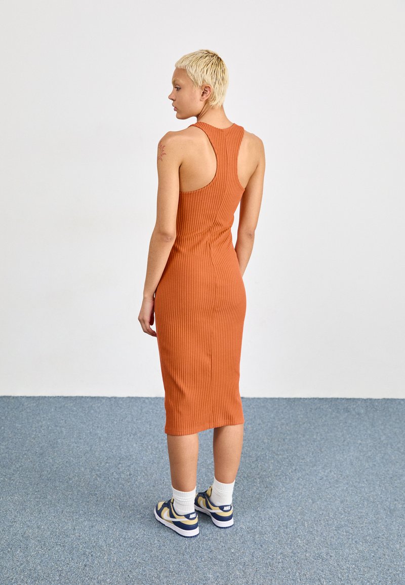 Vestido midi ajustado de canalé en naranja quemado, con un diseño de espalda nadadora. Combinado con calcetines blancos y zapatillas azul y amarillas.