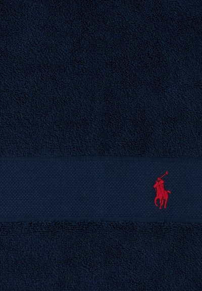 Dark navy blue textured fabric with a horizontal band featuring a small red embroidered polo player logo on horseback.
