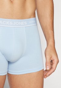Helle blaue Baumwoll-Boxershorts mit einem weißen elastischen Bund, auf dem die Marke "Jack & Jones" in einem wiederholenden Muster gedruckt ist.