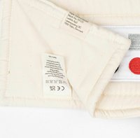 Cotton label with care instructions, featuring beige background, red and black accents. Includes CE mark for compliance.