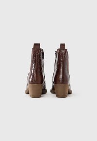 Brązowe botki ze skóry z tłoczeniem imitującym skórę krokodyla, na obcasie warstwowym, z bocznym zamkiem i detalem w postaci paska z tyłu. Gładka faktura i elegancki design.