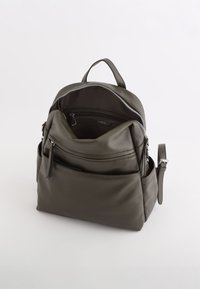 Sac à dos en cuir vert avec une forme structurée, doté d'une poignée supérieure, de compartiments zippés et d'une poche avant avec un détail de frange.