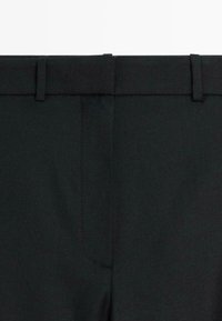Zwarte broek met een gladde textuur; heeft een platte tailleband en één achterzak. Getailleerd ontwerp met minimale details.