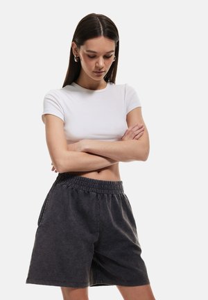 Sorte denimshorts med elastisk talje, sidelommer og en afslappet pasform, kombineret med en tætsiddende hvid t-shirt.