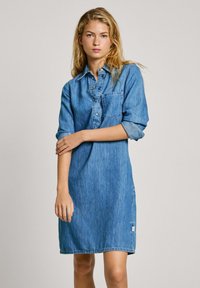 Denim srajčna obleka z ovratnim izrezom, sprednjim gumbnim zapiranjem, dolgimi zavitimi rokavi in žepom na blazini. Svetlo modra barva z gladko teksturo.