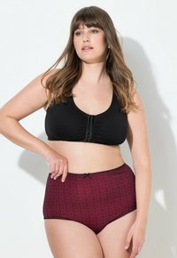 Reggiseno nero morbido con dettaglio arricciato sulla parte frontale e design con schienale a corsetto; abbinato a mutandine rosse a vita alta con motivo e pizzo nero.